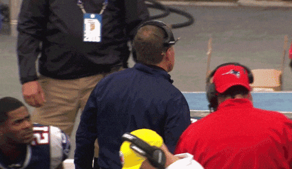 Football coach angrily throws a tablet while on the sidelines during a game, surrounded by other staff