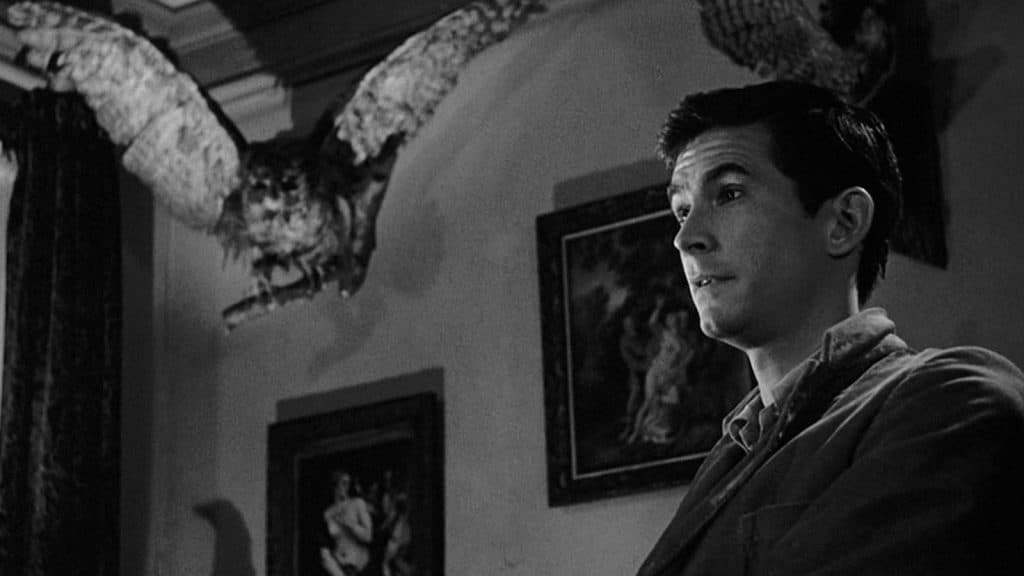 Norman Bates standing by a stuffed owl in Psycho.
