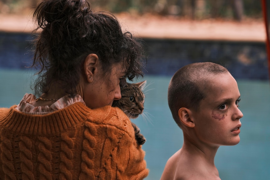 A woman holds a cat, standing next to a young boy in a drained pool.