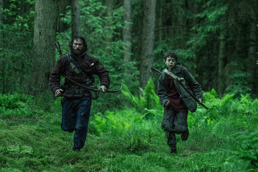 A man and a child armed with bows and arrows run through a forest