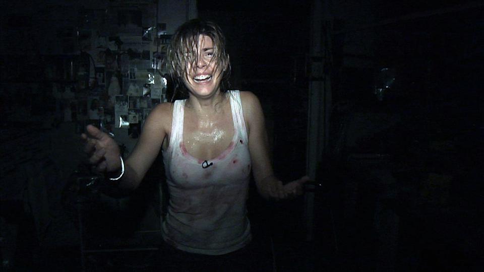 A woman in a white, bloody vest walks toward the camera.